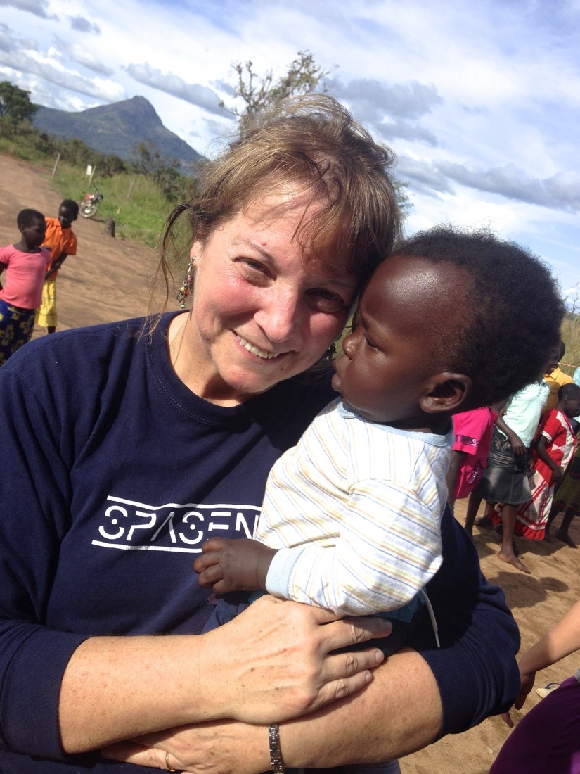 Mollie holding a small child outdoors, hills behind her